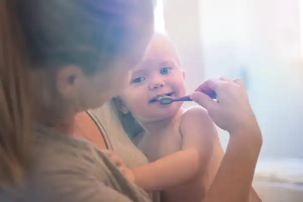 woman holding a young baby and attempting to brush the baby's teeth